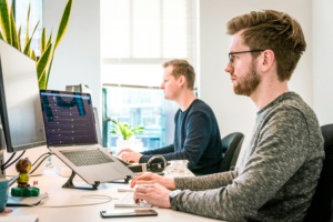 Two adults working at desks on computers in a bright office.