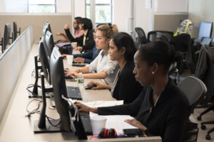 Learners seated in a computer lab working at desktop stations, focused on their screens.