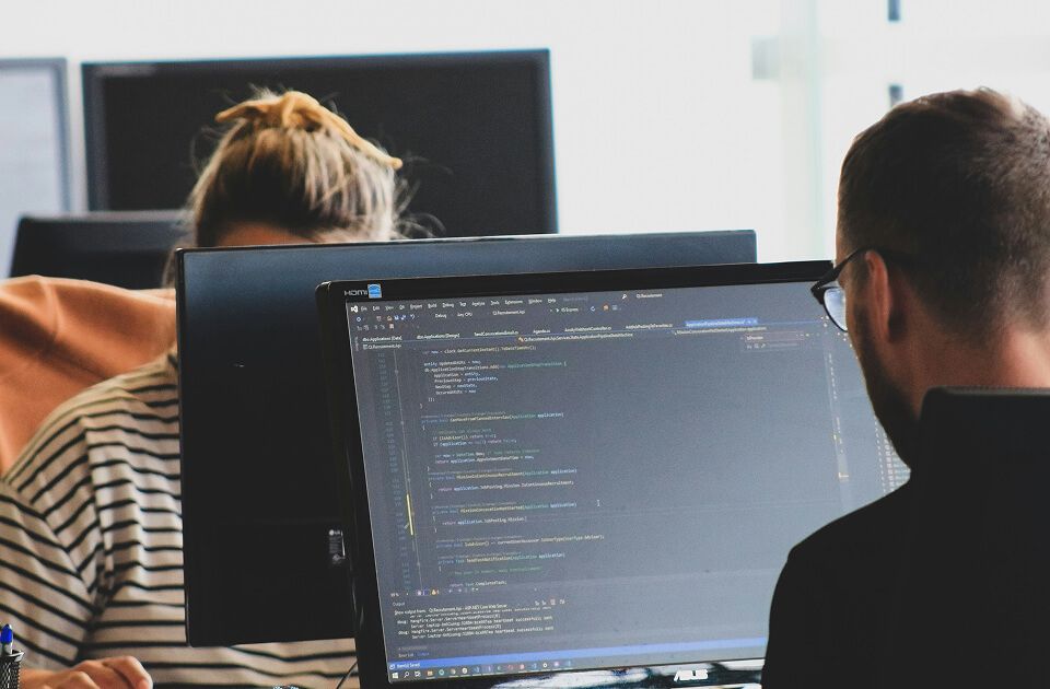 Man and woman viewing code on a monitor at a shared workstation in an office.