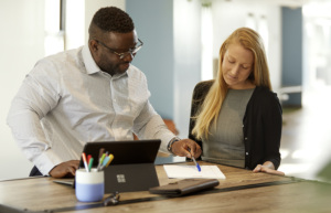 Instructor guiding an adult learner through paperwork at a table in a classroom-like workspace.