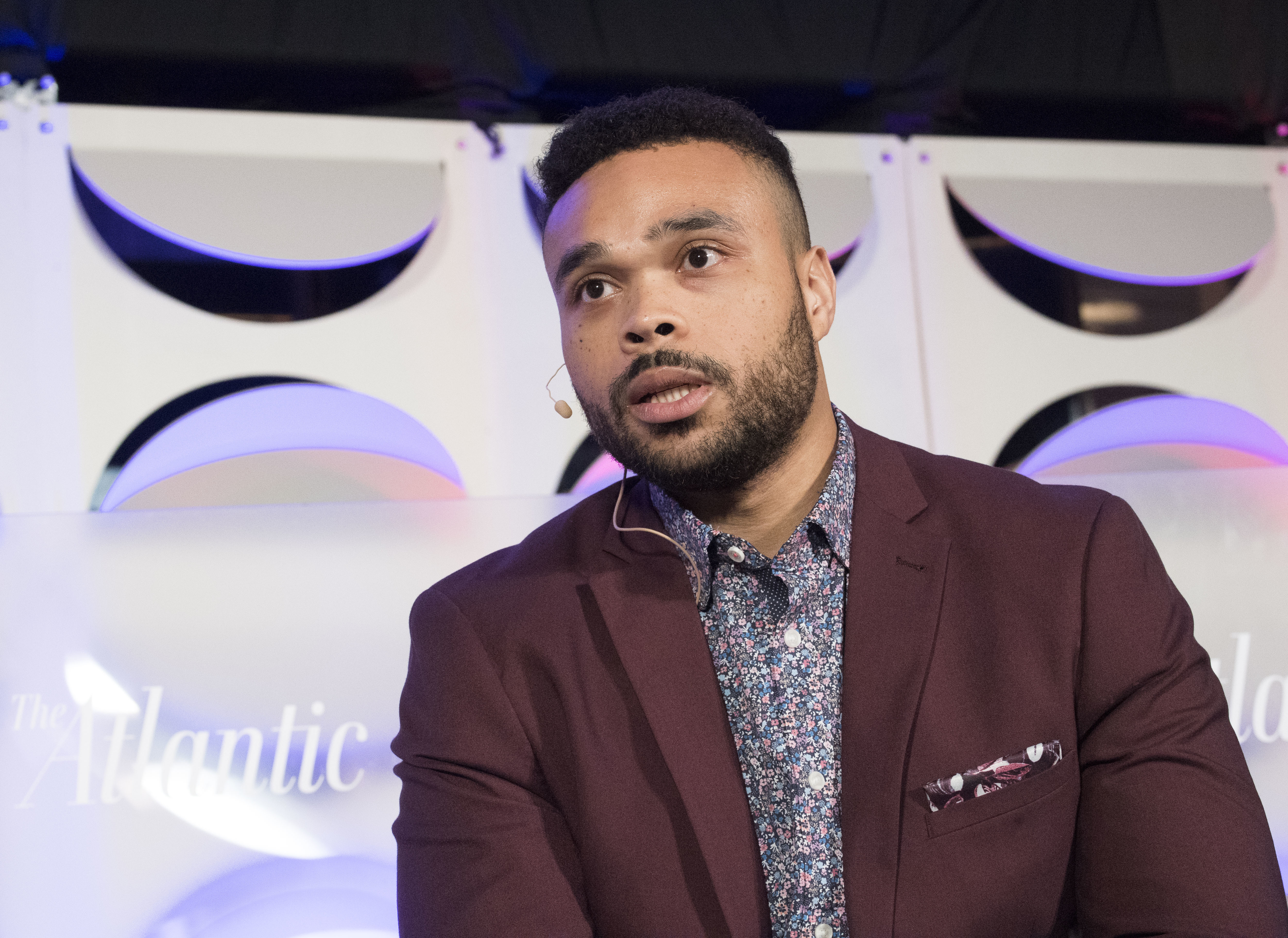 Man wearing a microphone speaking on a stage at a panel event.