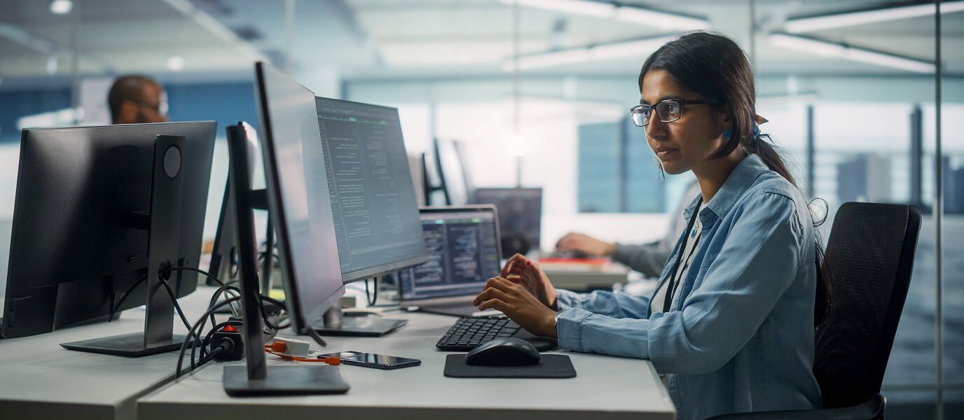 Employee in office workspace coding on computer at desk
