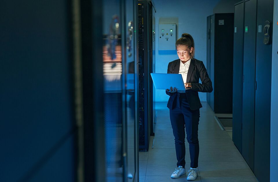 Female data center technician in data center on a laptop.