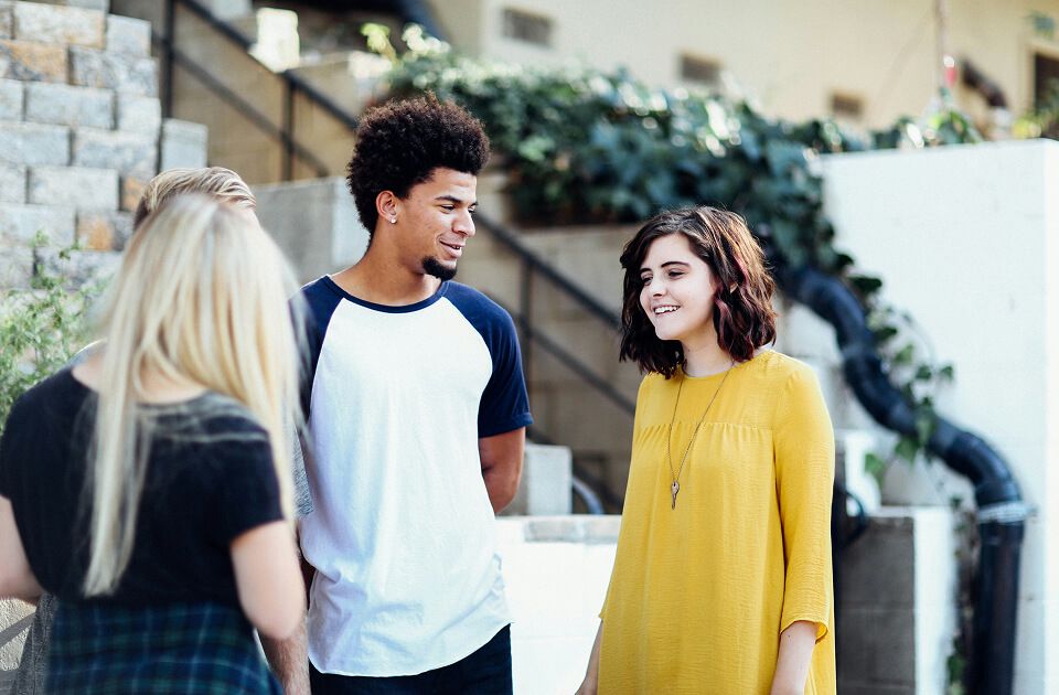 Three young adults networking, talking together outdoors near stone steps and greenery.