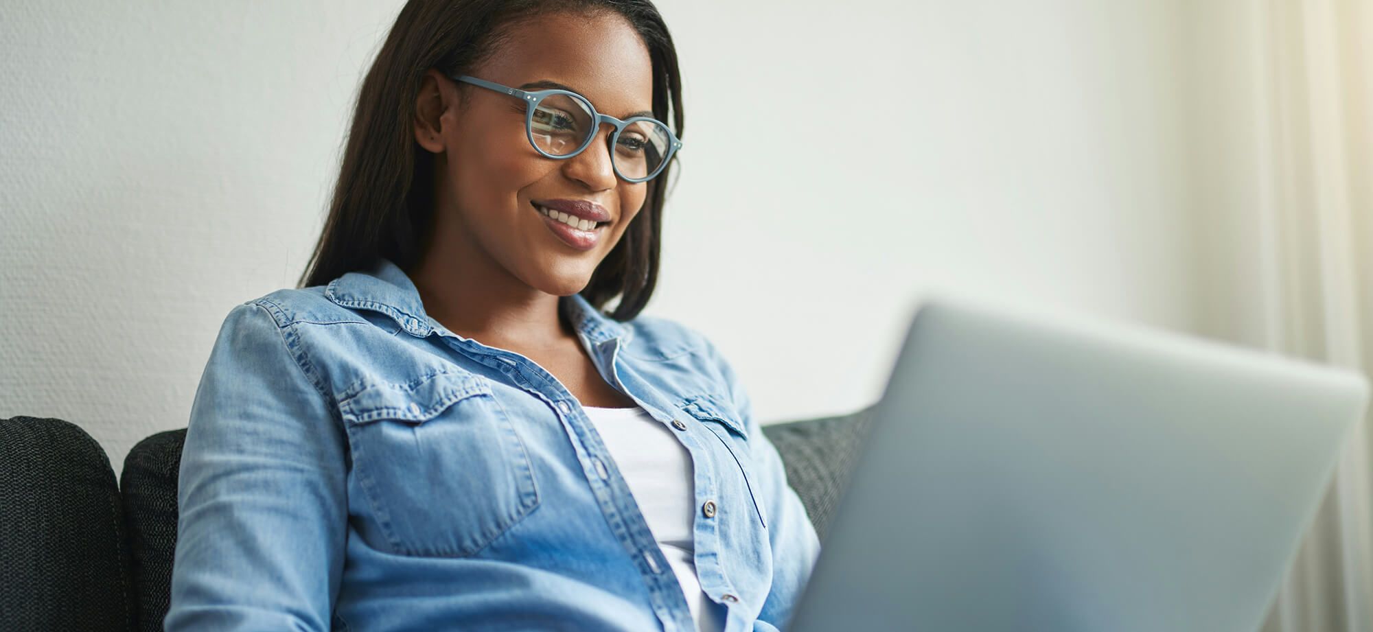 Woman seated on couch in home with laptop