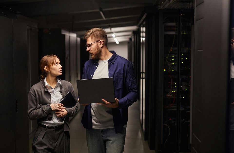 Two data center technicians talking beside server racks.