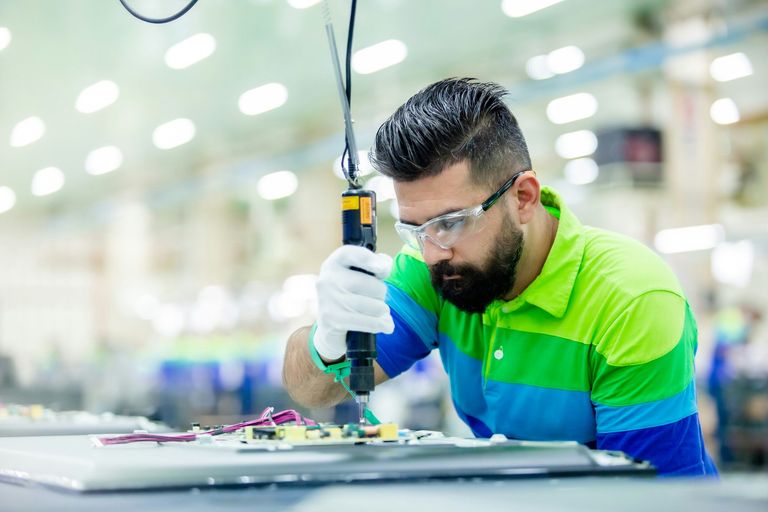 Manufacturing technician in safety glasses assembling components with a powered driver on a factory floor