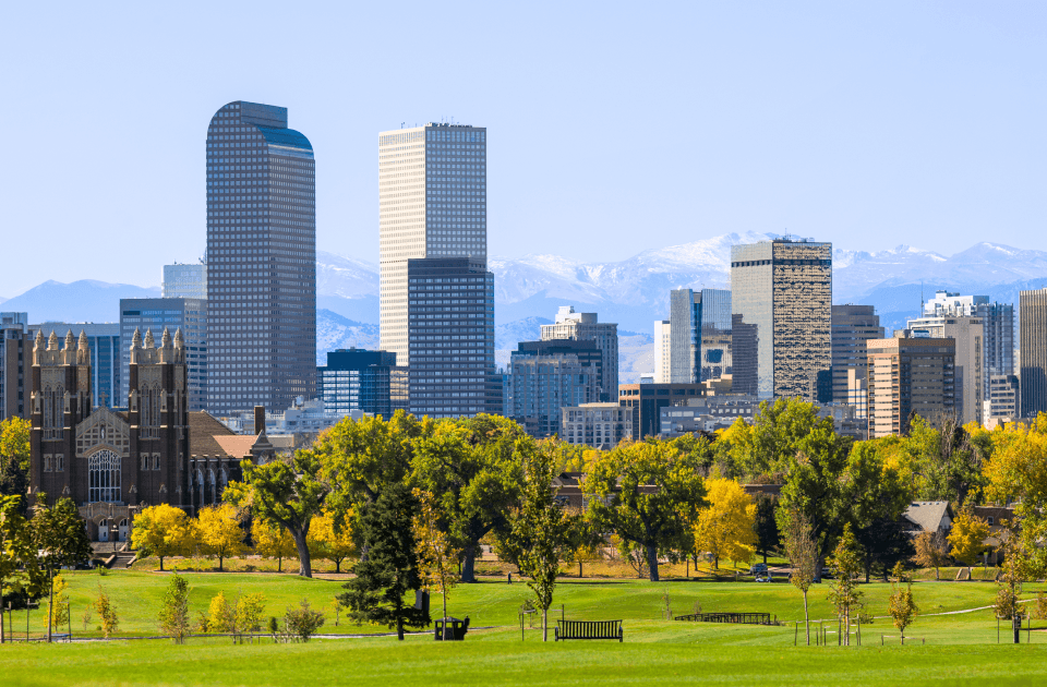 Denver skyline overlooking a green park with the Rocky Mountains in the background.
