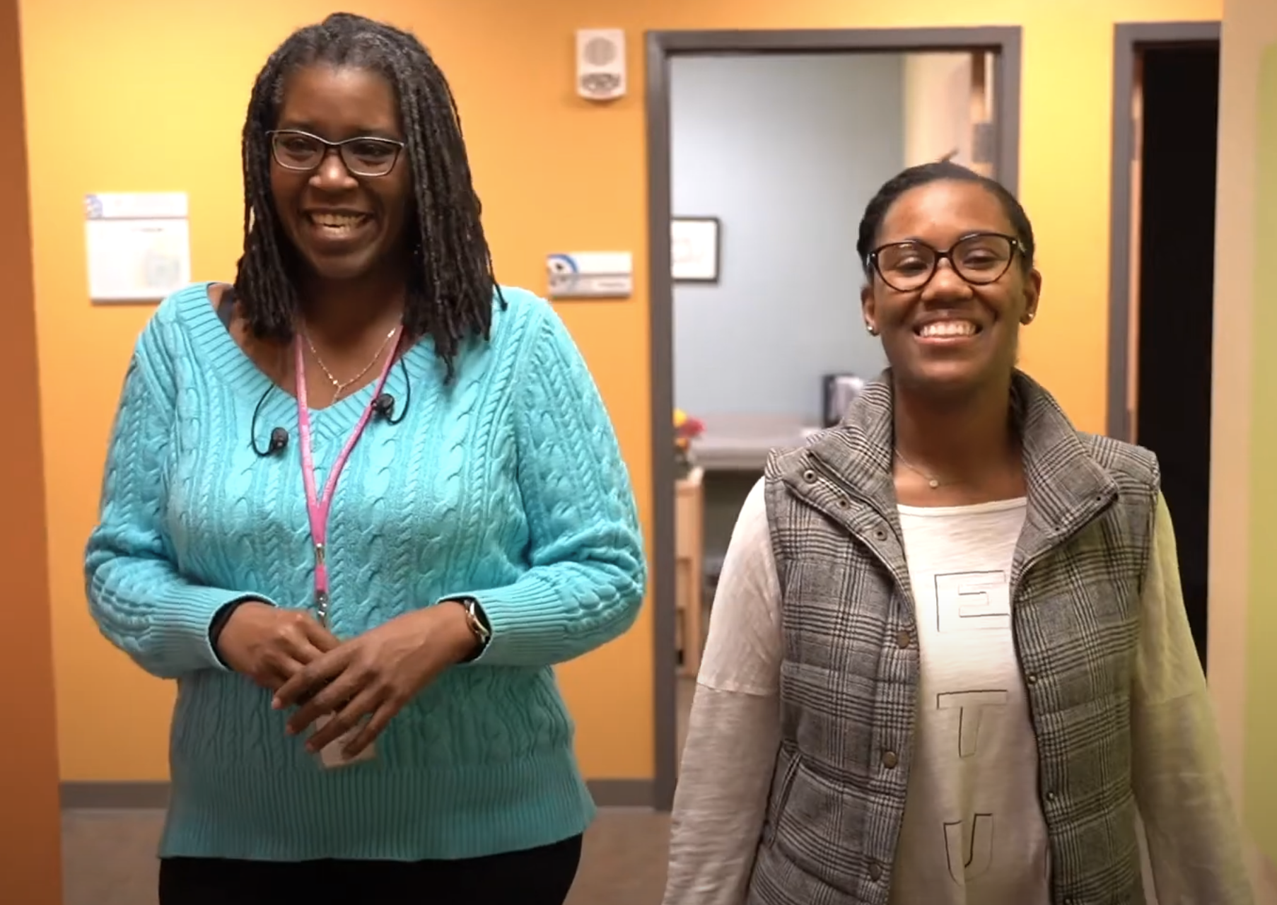 Two women in an orange hallway walking and smiling